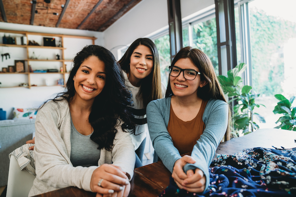 Portrait of three young adult hispanic women smiling together. They are looking at camera.