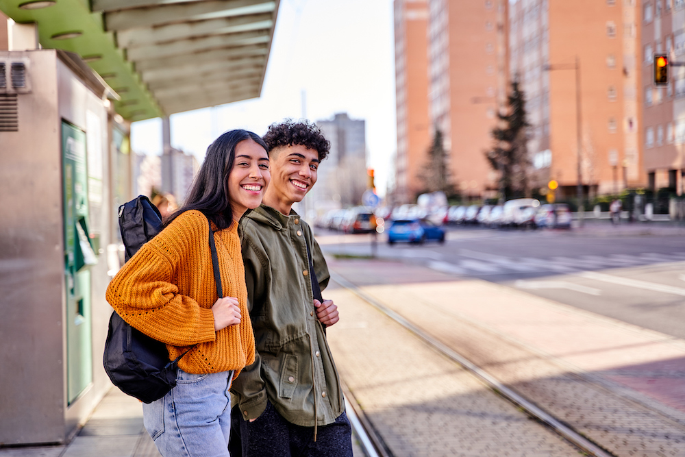 teenage couple waiting at the train or tram stop. young students with a guitar and a ukulele in its case.